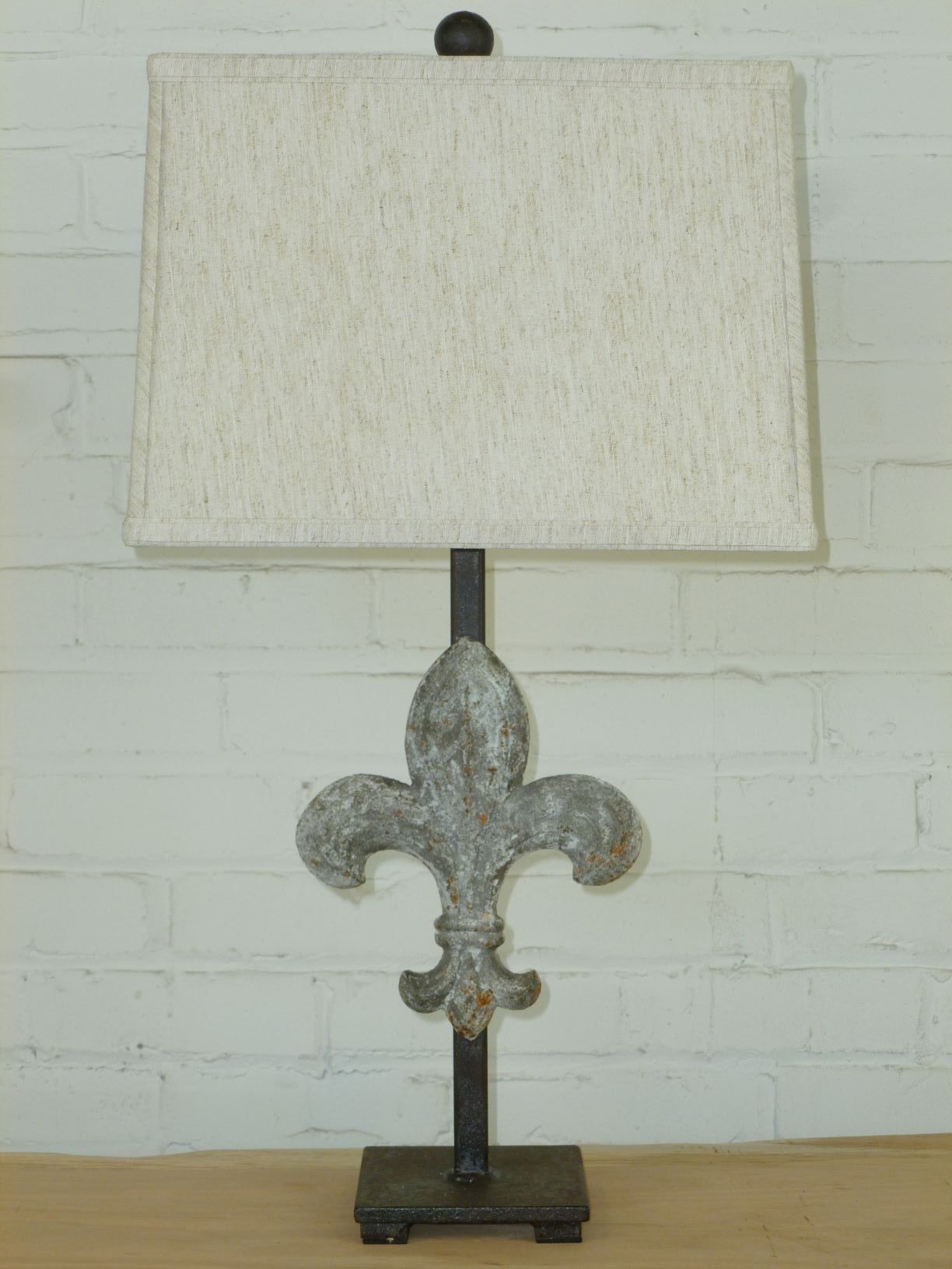 Ferro Designs LLC fleur-de-lis custom iron table lamp with a gray, distressed finish and a dark iron base. Paired with a 14 inch rectangle linen lamp shade.