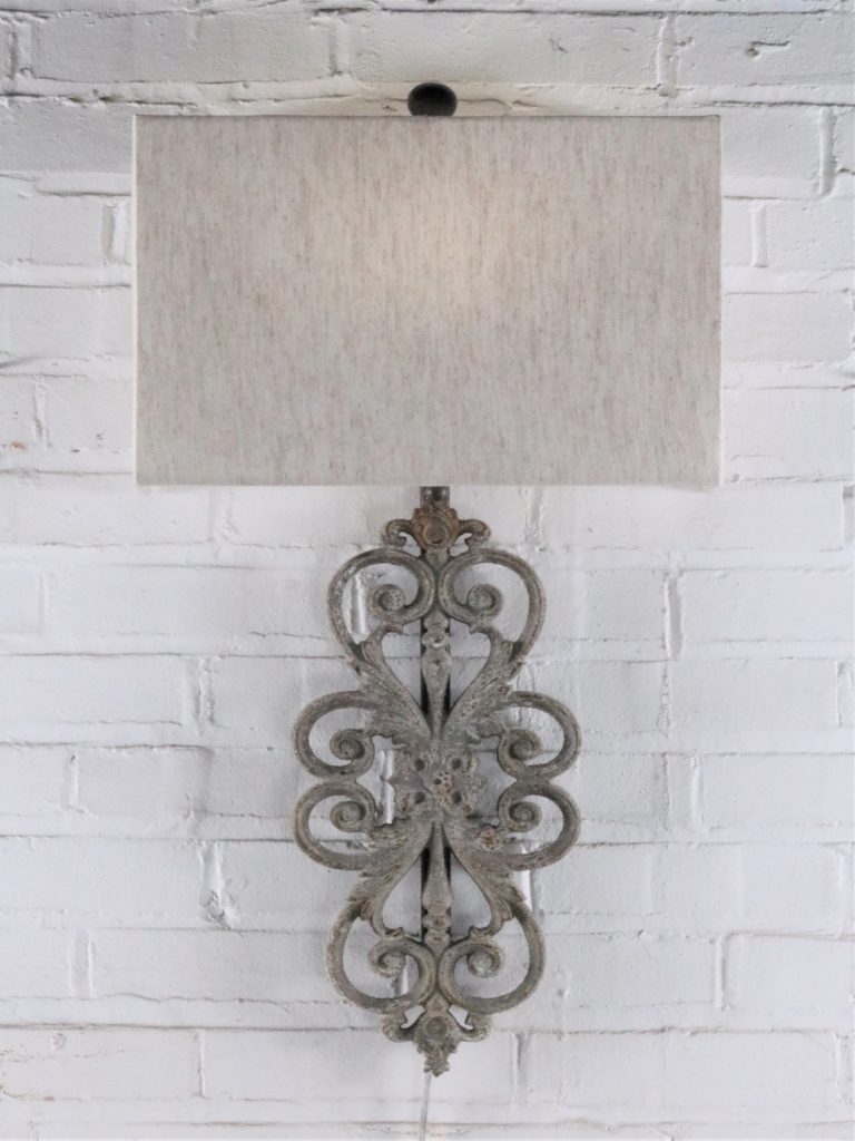 Scrollwork custom iron wall sconce with a gray, distressed finish. Paired with a half rectangle linen lamp shade.